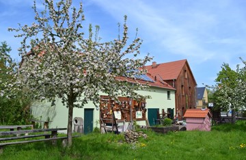 Grüne Welle Umweltverein e.V. | Ökologische Station Naundorf Naturhof mit Nistkästen an der Wand sowie einer Wiese mit blühenden Bäumen