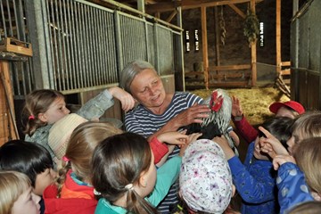Reit- und Kinderbauernhof Krasselt Frau Krasselt auf ihrem Hof mit einem Huhn in der Hand und umgeben von Kindern