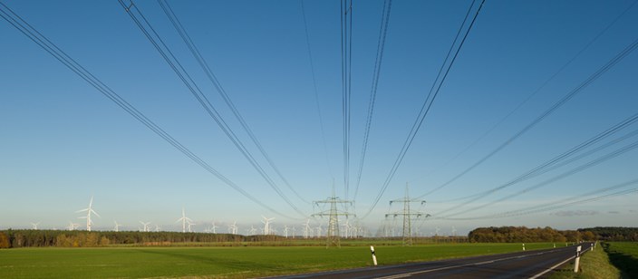 Stromleitungen über eine Straße, im Hintergrund Windräder Stromleitungen über eine Straße, im Hintergrund Windräder